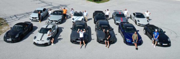 12 Autos stehen in zwei Reihen und die Fahrer stehen davor von der Tour Kurvenjagd
